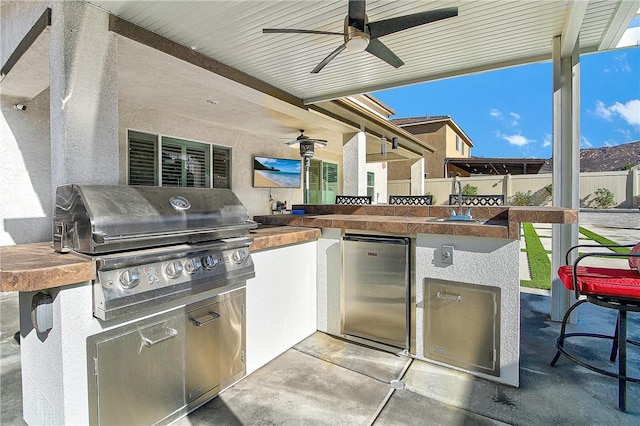 view of patio featuring exterior kitchen, grilling area, an outdoor wet bar, and ceiling fan