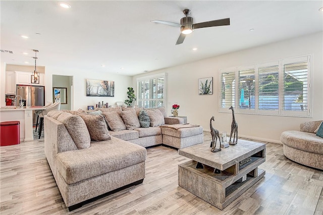 living room with ceiling fan with notable chandelier and light hardwood / wood-style flooring