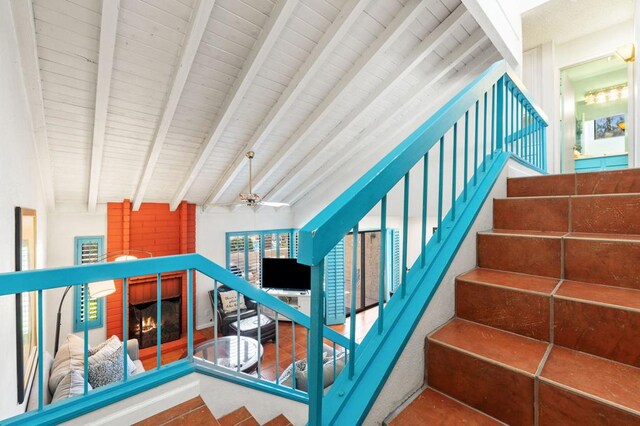 stairway featuring ceiling fan, a large fireplace, and lofted ceiling with beams