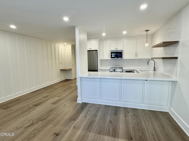 kitchen featuring hardwood / wood-style floors, white cabinets, hanging light fixtures, kitchen peninsula, and stainless steel appliances