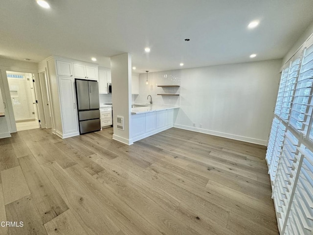 kitchen with kitchen peninsula, stainless steel appliances, white cabinetry, and light hardwood / wood-style flooring