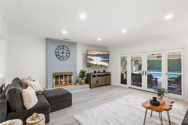 living room with a brick fireplace, ornamental molding, light hardwood / wood-style flooring, and french doors