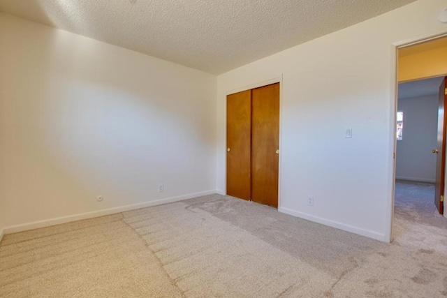 unfurnished bedroom featuring light colored carpet, a textured ceiling, and a closet