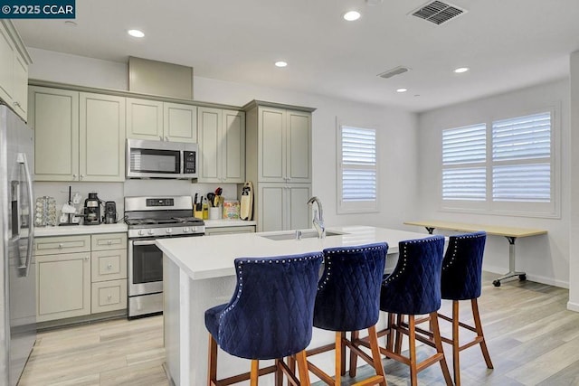 kitchen with a kitchen bar, stainless steel appliances, sink, light wood-type flooring, and a center island with sink