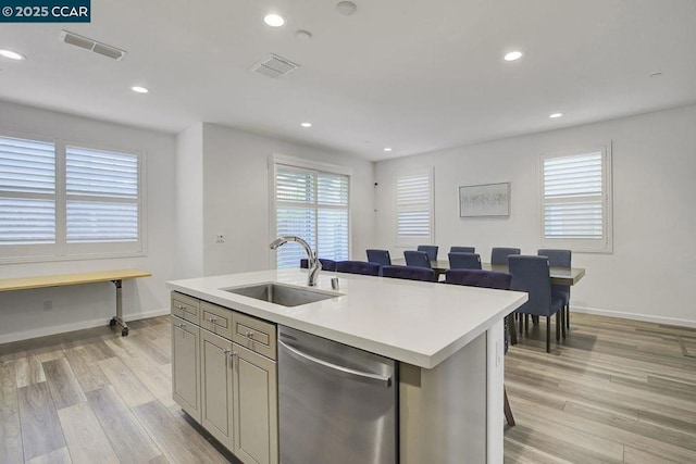 kitchen with a kitchen bar, a kitchen island with sink, stainless steel dishwasher, light hardwood / wood-style flooring, and sink