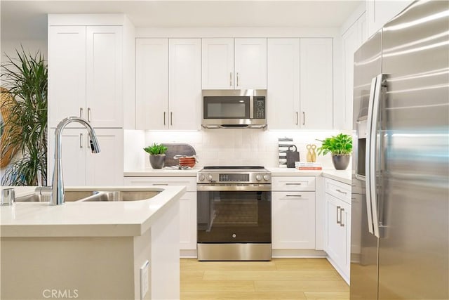 kitchen with white cabinets, sink, stainless steel appliances, and light hardwood / wood-style flooring