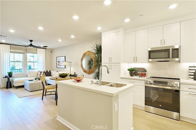 kitchen featuring white cabinets, sink, light wood-type flooring, an island with sink, and stainless steel appliances