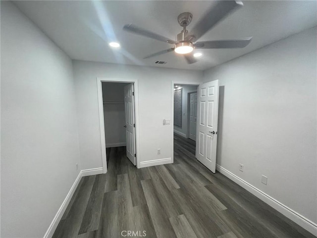 unfurnished bedroom featuring a walk in closet, dark hardwood / wood-style floors, a closet, and ceiling fan