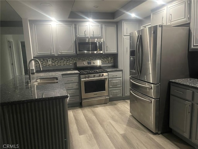 kitchen featuring appliances with stainless steel finishes, light wood-type flooring, gray cabinetry, dark stone counters, and sink