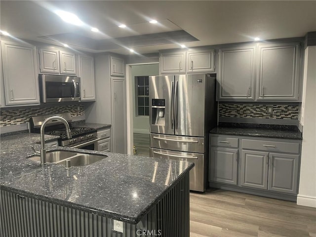 kitchen featuring backsplash, dark stone counters, gray cabinetry, stainless steel appliances, and light hardwood / wood-style floors