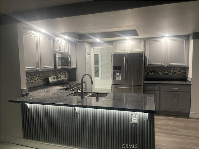 kitchen with kitchen peninsula, light wood-type flooring, dark stone counters, stainless steel appliances, and sink