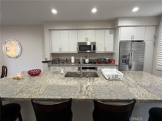 kitchen with a kitchen breakfast bar, a spacious island, sink, light stone countertops, and appliances with stainless steel finishes