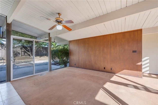 empty room featuring floor to ceiling windows, wooden walls, ceiling fan, tile patterned flooring, and vaulted ceiling with beams