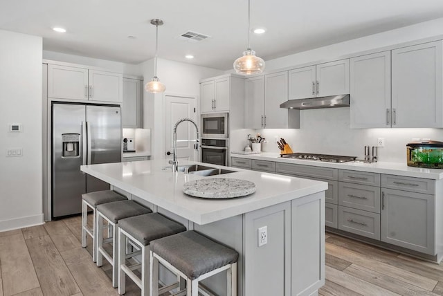 kitchen with pendant lighting, sink, stainless steel appliances, and light hardwood / wood-style flooring