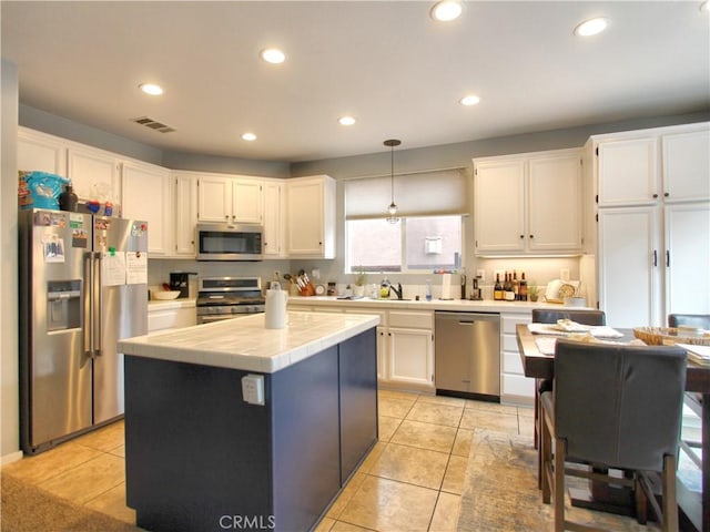 kitchen with stainless steel appliances, a kitchen island, tile countertops, decorative light fixtures, and white cabinets