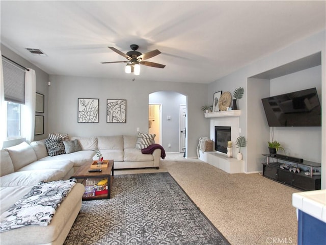 living room featuring ceiling fan, carpet floors, and a tiled fireplace