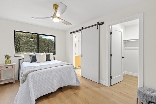 bedroom featuring a barn door, ceiling fan, light wood-type flooring, a closet, and a walk in closet