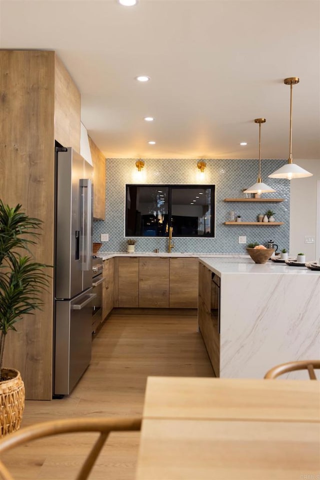 kitchen with appliances with stainless steel finishes, decorative light fixtures, tasteful backsplash, light hardwood / wood-style floors, and sink