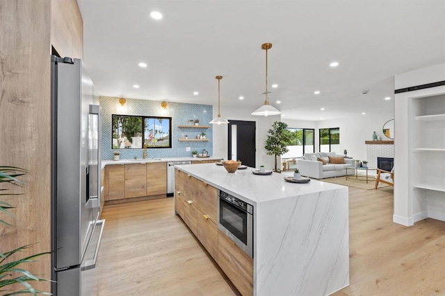 kitchen with light hardwood / wood-style floors, appliances with stainless steel finishes, a spacious island, a fireplace, and hanging light fixtures