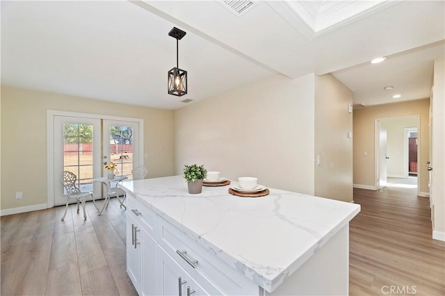 kitchen with light stone counters, white cabinets, light hardwood / wood-style floors, a kitchen island, and hanging light fixtures