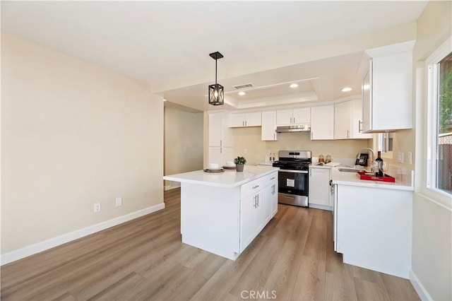 kitchen featuring a raised ceiling, decorative light fixtures, white cabinets, a center island, and stainless steel stove