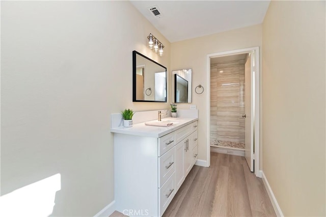 bathroom with tiled shower, vanity, and hardwood / wood-style flooring