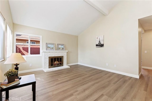 living room featuring beam ceiling, high vaulted ceiling, light hardwood / wood-style floors, and a brick fireplace