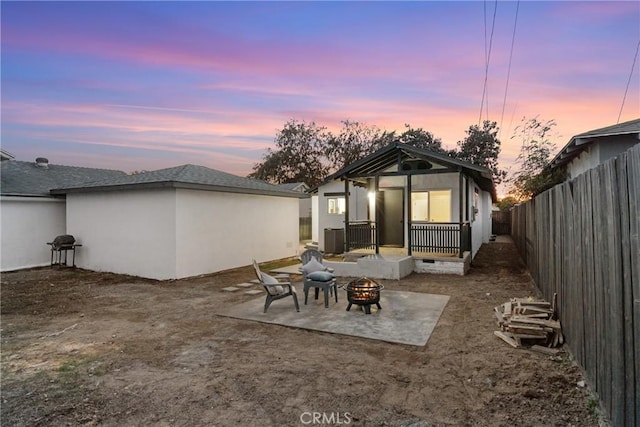 back house at dusk featuring an outdoor fire pit, cooling unit, and a patio area