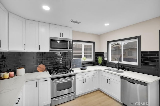 kitchen featuring sink, white cabinetry, light hardwood / wood-style flooring, appliances with stainless steel finishes, and light stone counters