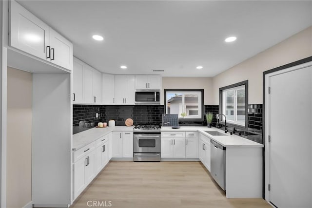 kitchen with appliances with stainless steel finishes, backsplash, light wood-type flooring, white cabinets, and sink