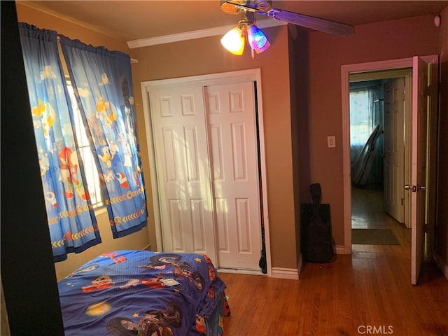 bedroom with hardwood / wood-style floors, a closet, ceiling fan, and crown molding