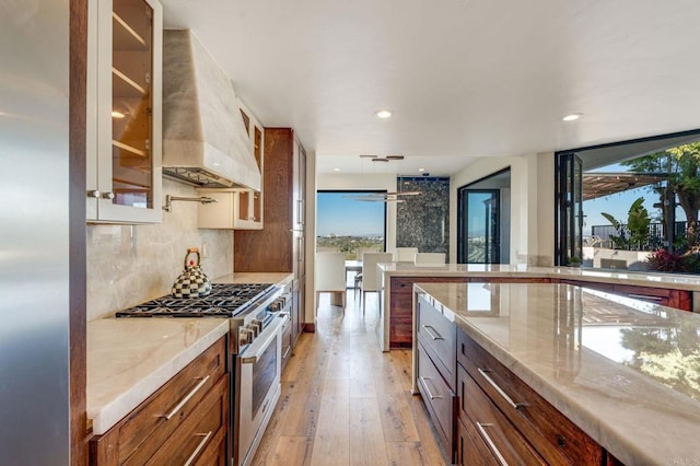 kitchen with stainless steel stove, custom exhaust hood, light stone countertops, and decorative backsplash