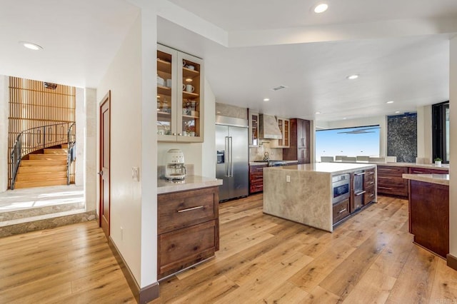 kitchen featuring built in fridge, a center island, tasteful backsplash, light hardwood / wood-style flooring, and wall chimney exhaust hood