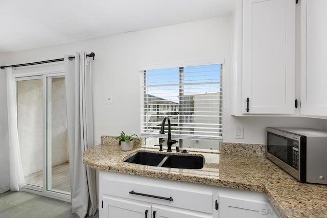 kitchen with light tile patterned floors, white cabinetry, light stone counters, and sink