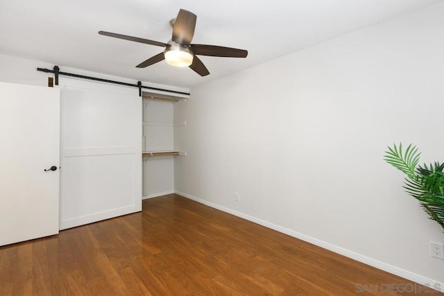 unfurnished bedroom featuring ceiling fan, hardwood / wood-style floors, a closet, and a barn door