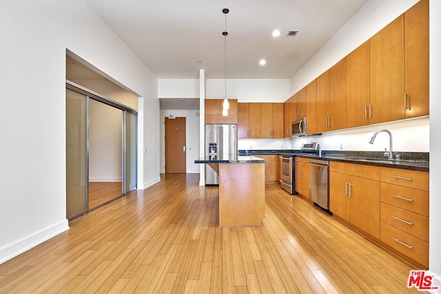 kitchen featuring a center island, sink, hanging light fixtures, light hardwood / wood-style flooring, and stainless steel appliances