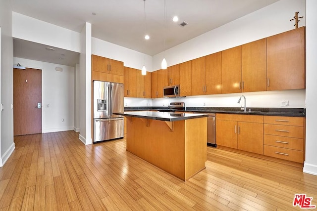 kitchen featuring stainless steel appliances, sink, pendant lighting, light hardwood / wood-style flooring, and a kitchen island