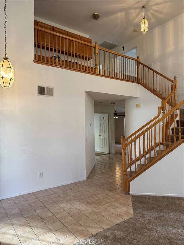 stairs with ceiling fan, tile patterned flooring, and a high ceiling