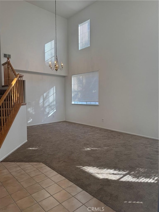 unfurnished living room featuring an inviting chandelier, a towering ceiling, and carpet flooring