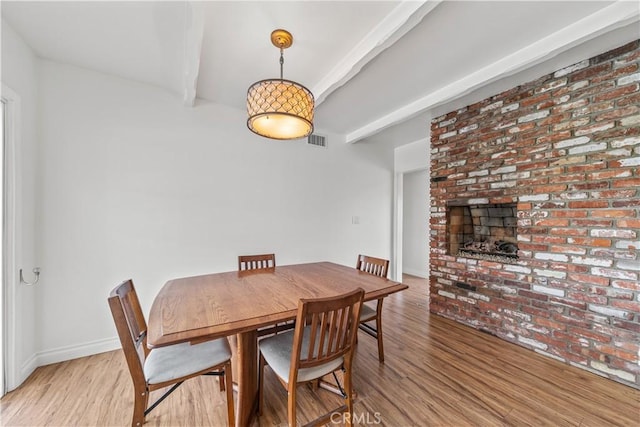 dining room featuring beam ceiling, light hardwood / wood-style floors, and a brick fireplace