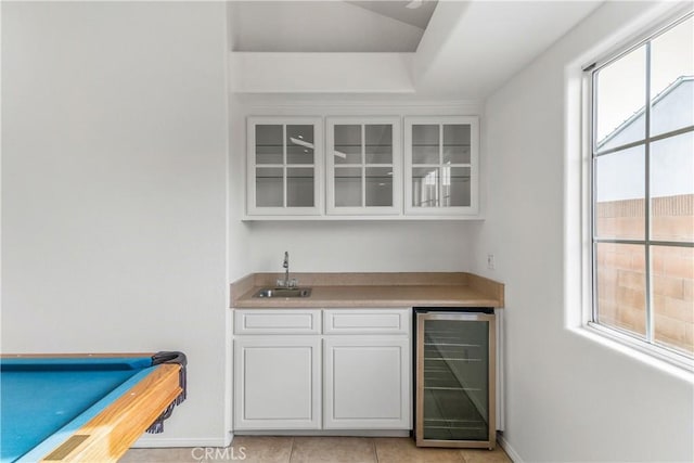 bar with beverage cooler, sink, light tile patterned floors, white cabinets, and pool table