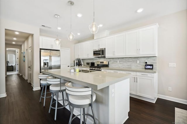 kitchen with decorative backsplash, an island with sink, appliances with stainless steel finishes, decorative light fixtures, and white cabinetry