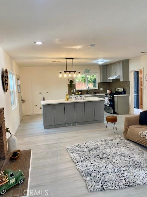 kitchen with decorative backsplash, a brick fireplace, stainless steel range, pendant lighting, and gray cabinets