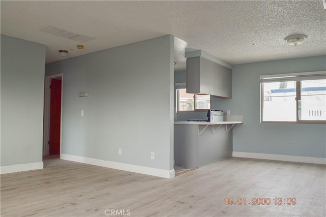 kitchen with kitchen peninsula, a textured ceiling, a breakfast bar, and light hardwood / wood-style floors