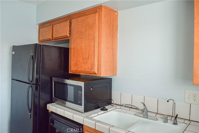 kitchen with black refrigerator, sink, dishwasher, tile patterned flooring, and tile counters