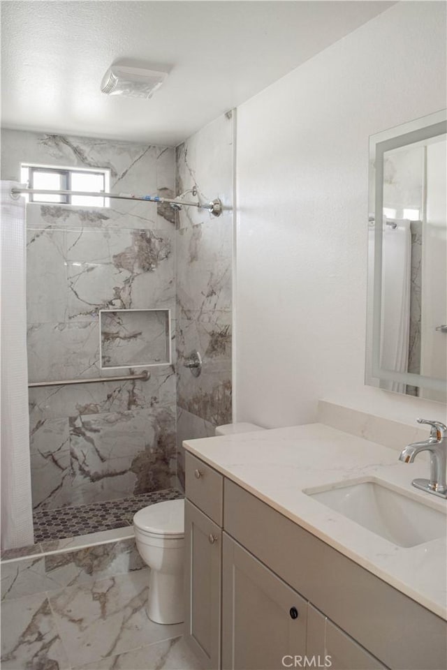 bathroom with tiled shower, vanity, and toilet