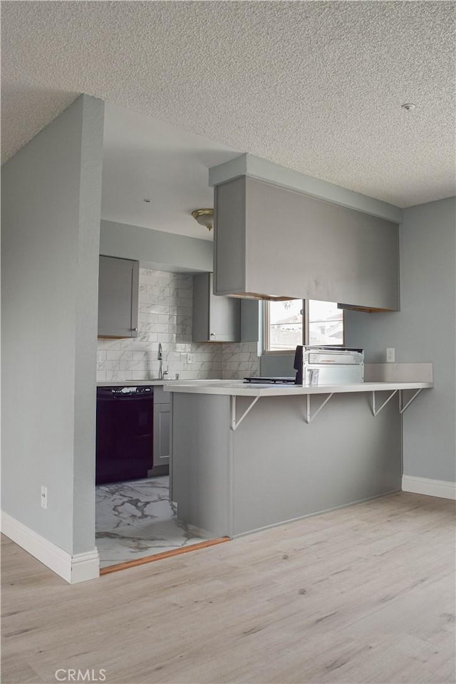 kitchen with a kitchen bar, a textured ceiling, gray cabinets, and dishwasher