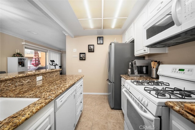 kitchen featuring white appliances, dark stone counters, sink, light tile patterned floors, and white cabinetry