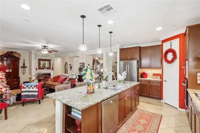 kitchen featuring appliances with stainless steel finishes, a large fireplace, sink, hanging light fixtures, and an island with sink