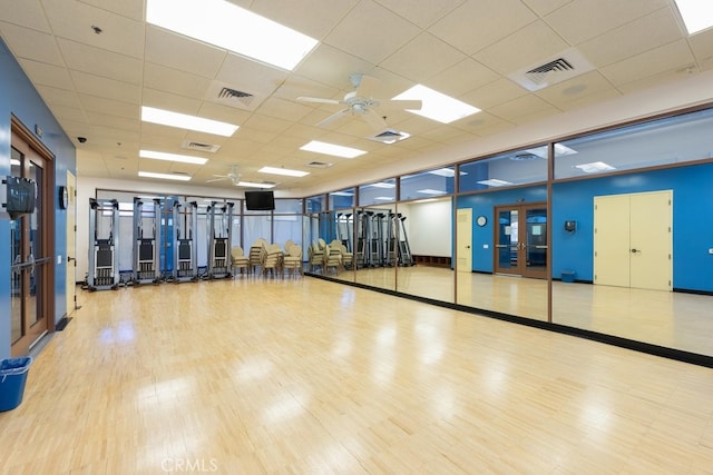 workout area featuring ceiling fan, a drop ceiling, light hardwood / wood-style floors, and french doors